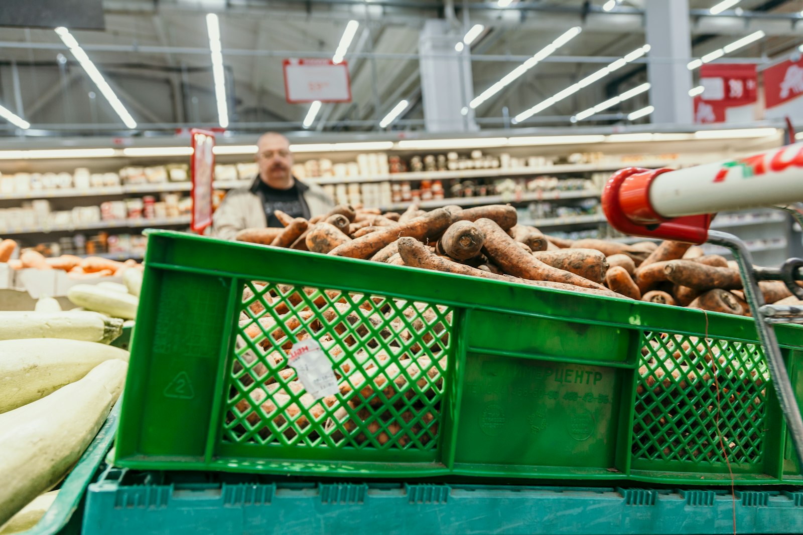 Caisses vertes de légumes dans l'allée d'un supermarché, un employé en arrière-plan